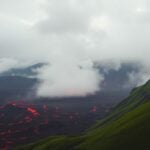 Dramatic volcano landscape with green hills and mist.